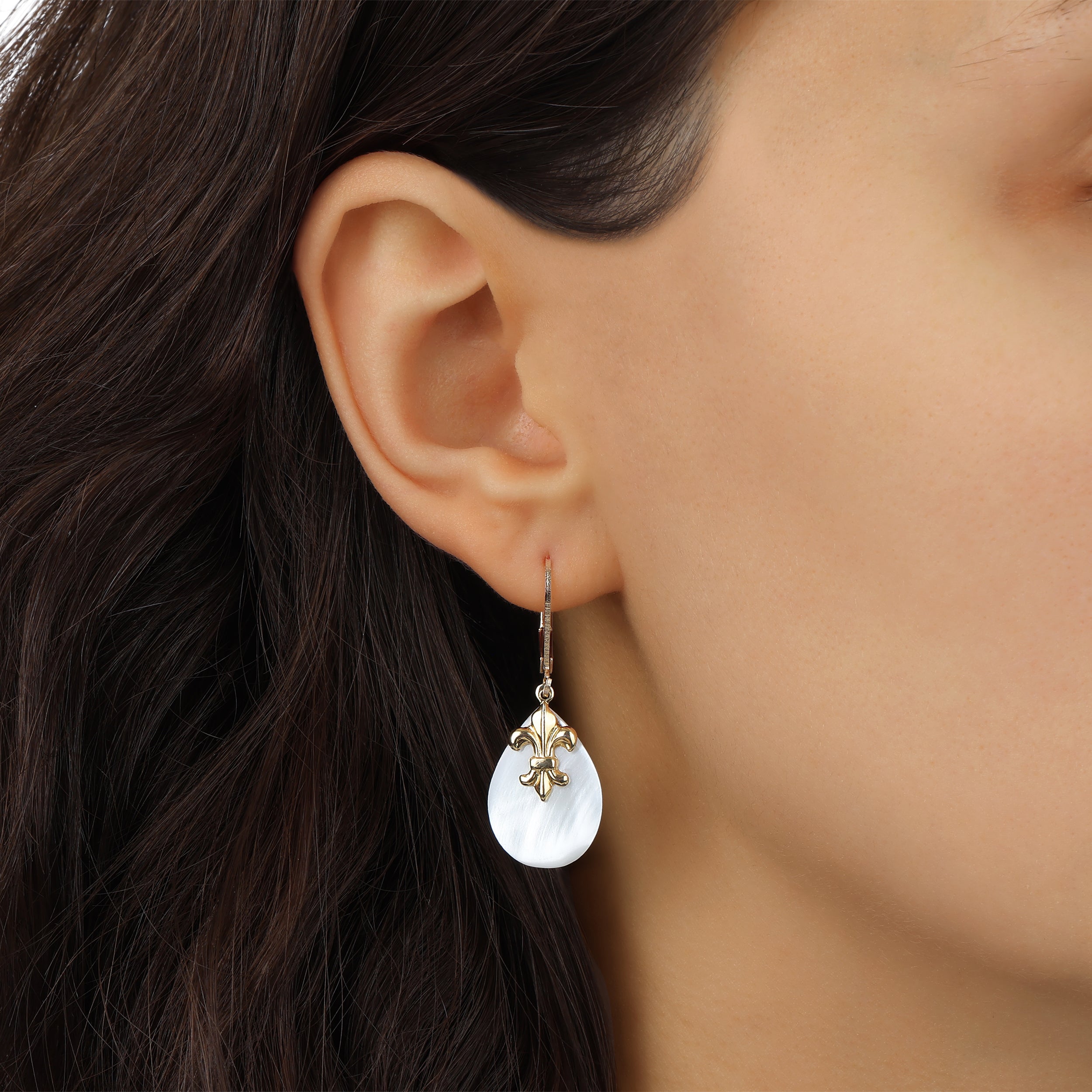 A close-up of a model's ear wearing an Oval Imitation Mother of Pearl & Gold Fleur De Lis Drop Earrings