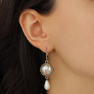 A close-up of a model's ear wearing a Round Pink Floral Decal & Faux Pearl Teardrop Dangle Earrings