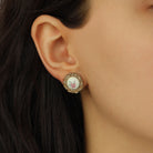 A close-up of a woman's ear wearing Golden Round Cream Stone & Pink Flower Decal Stud Earrings