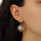 A close-up of a model's ear wearing Pink Porcelain Rose Filigree Drop Earrings