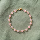 Light Rose Pink Beaded Bracelet displayed on a textured sage green fabric background.