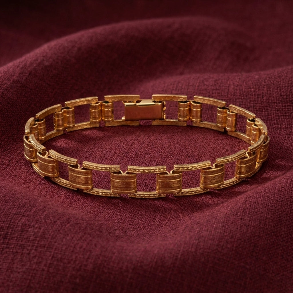 A gold-toned metal link bracelet with a textured geometric design, displayed on a draped burgundy fabric background.