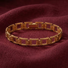 A gold-toned metal link bracelet with a textured geometric design, displayed on a draped burgundy fabric background.