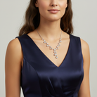 Woman wearing a navy blue dress with a silver necklace against a neutral background.