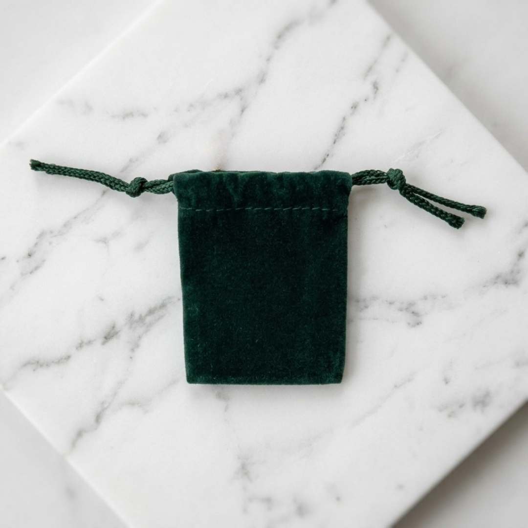 Green velvet drawstring jewelry pouch resting on white marble stone