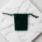 Green velvet drawstring jewelry pouch resting on white marble stone