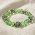 Green Fire Polished Flower Bead & Crystal Stretch Bracelet displayed on a textured beige fabric background.