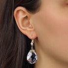 A close-up of a person's ear wearing a gold tone Multi-Faceted Clear Briolette Crystal Stone Drop & Dangle Earrings