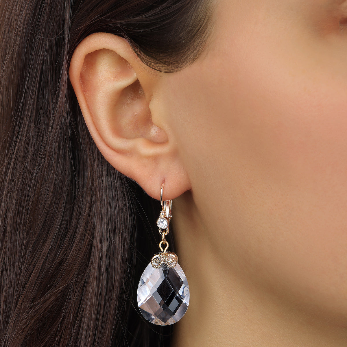 A close-up of a person's ear wearing a gold tone Multi-Faceted Clear Briolette Crystal Stone Drop & Dangle Earrings