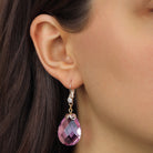 A close-up of a woman's ear wearing a Gold Tone Multi-Faceted Pink Briolette Crystal Stone Drop & Dangle Earrings