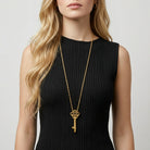 Woman wearing a black dress with a gold key-shaped whistle necklace on a plain background