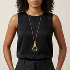 Woman in a black outfit wearing a gold necklace with a cat magnifying glass pendant.