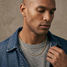 Man wearing a denim jacket over a gray sweater against a neutral background