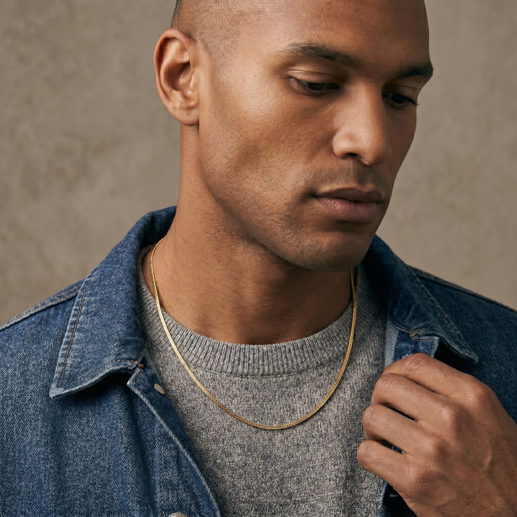 Man wearing a denim jacket over a gray sweater against a neutral background