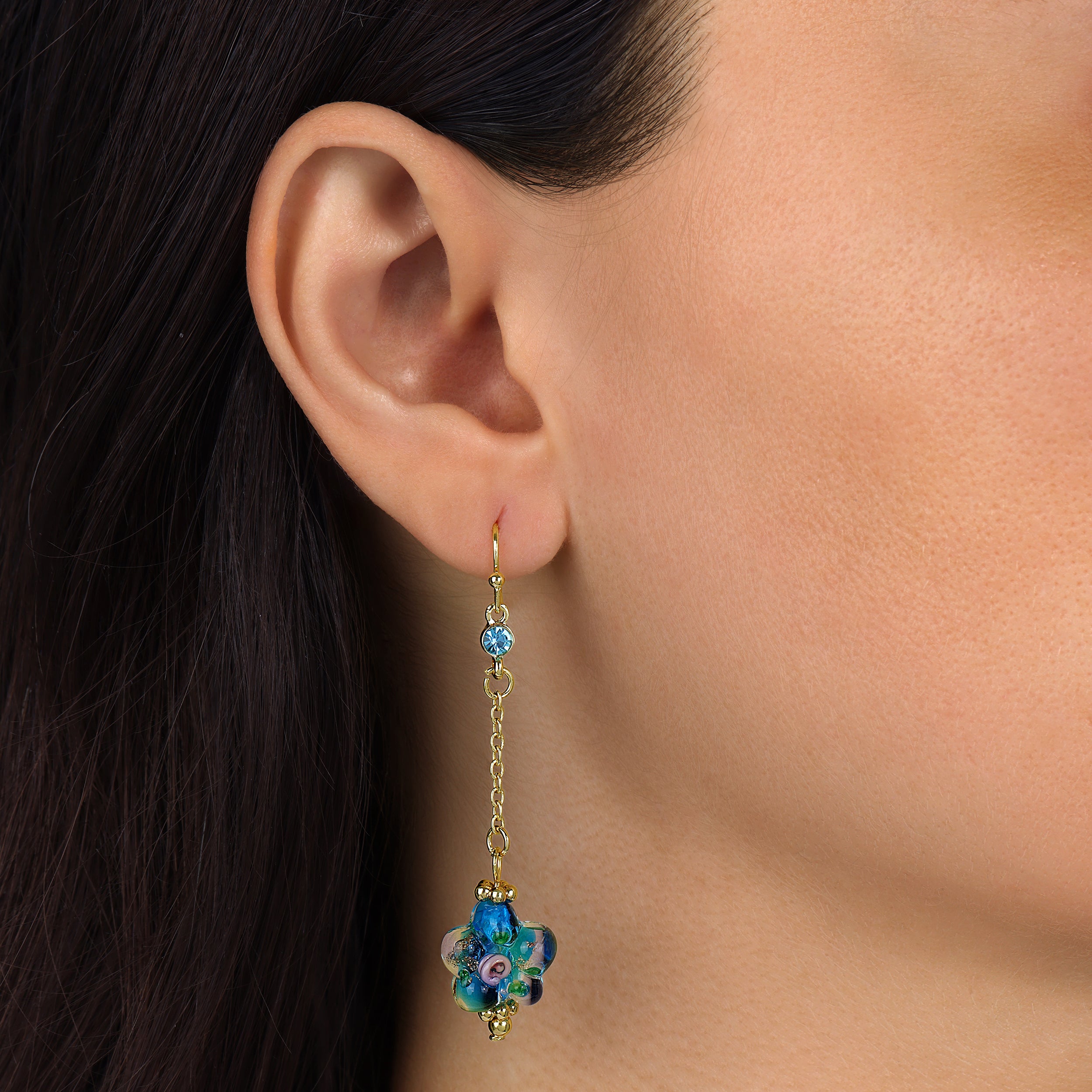 A close-up of a model's ear wearing a Blue Blooming Flower Bead & Crystal Dangle Earrings
