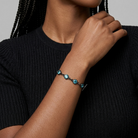 Person wearing a black sweater with a blue beaded bracelet on a neutral background