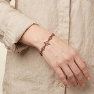 Hand wearing a bracelet with pink stones against a beige background
