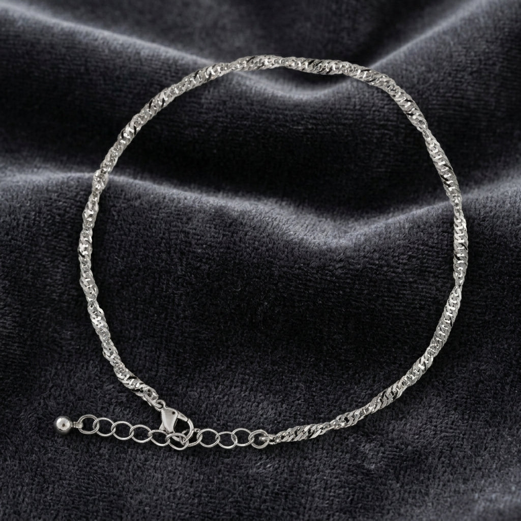 Silver tone twisted anklet resting on dark fabric