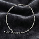 Silver tone twisted anklet resting on dark fabric