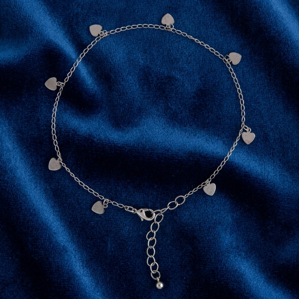 Silver tone anklet with heart charms resting on dark blue fabric