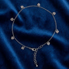 Silver tone anklet with heart charms resting on dark blue fabric