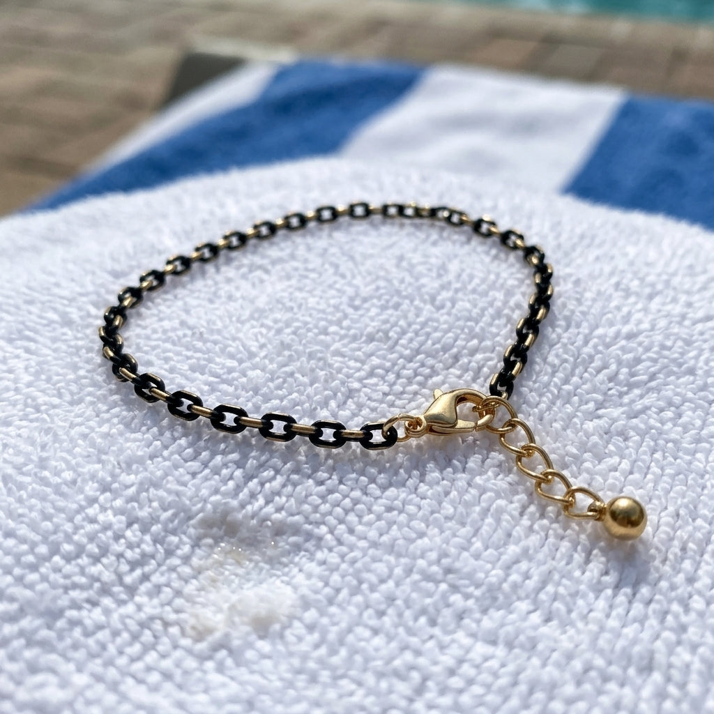 Gold and black chain anklet on a white towel with blue stripes.