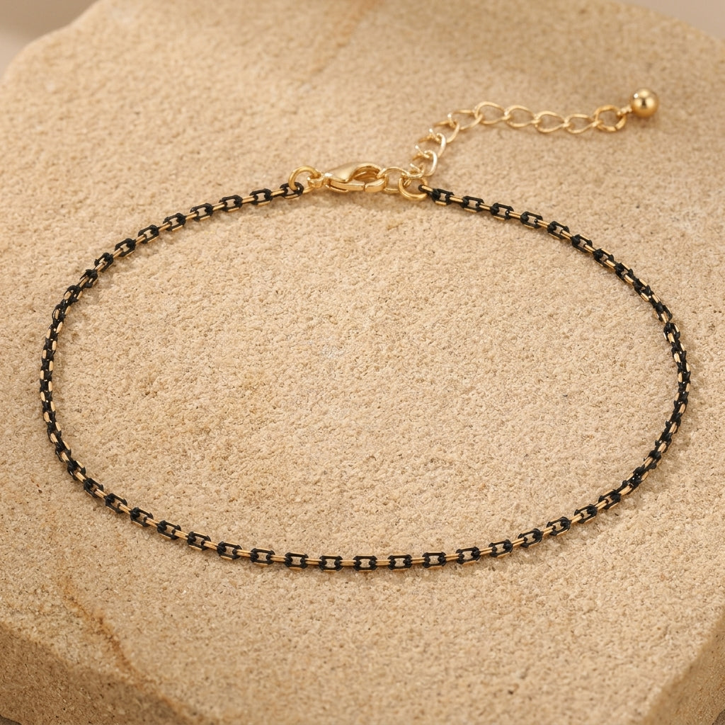 Black and gold tone anklet resting on beige stone
