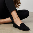 Woman in black pants and black loafers wearing a gold and black tone anklet