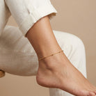 Woman in white linen pants showing off her gold tone beaded anklet