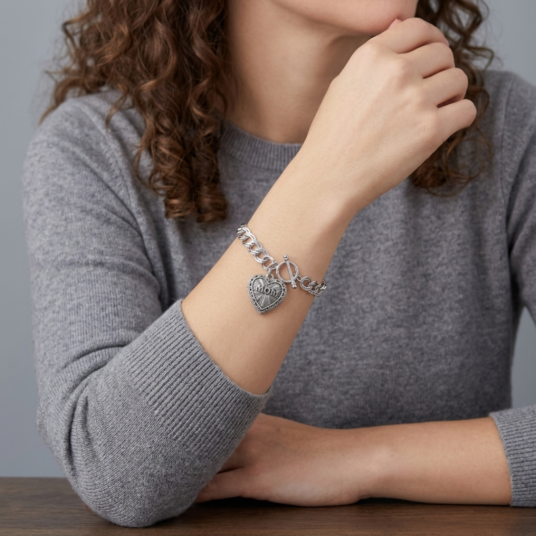 Person wearing a silver bracelet with a heart-shaped "MOM" charm on a gray background