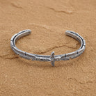 Pewter Totem Pole Feather Cuff Bracelet displayed on a textured sandy surface.