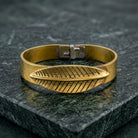 Gold tone BoHo style bracelet with feather design on a dark stone surface