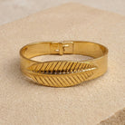 Gold Feather T.R.U. Bangle Bracelet displayed on a beige textured surface.