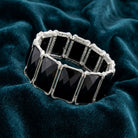 Black stone bracelet with silver tone accents resting on dark blue fabric