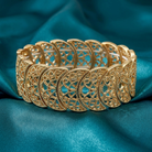 Gold bracelet with intricate design on a blue satin background