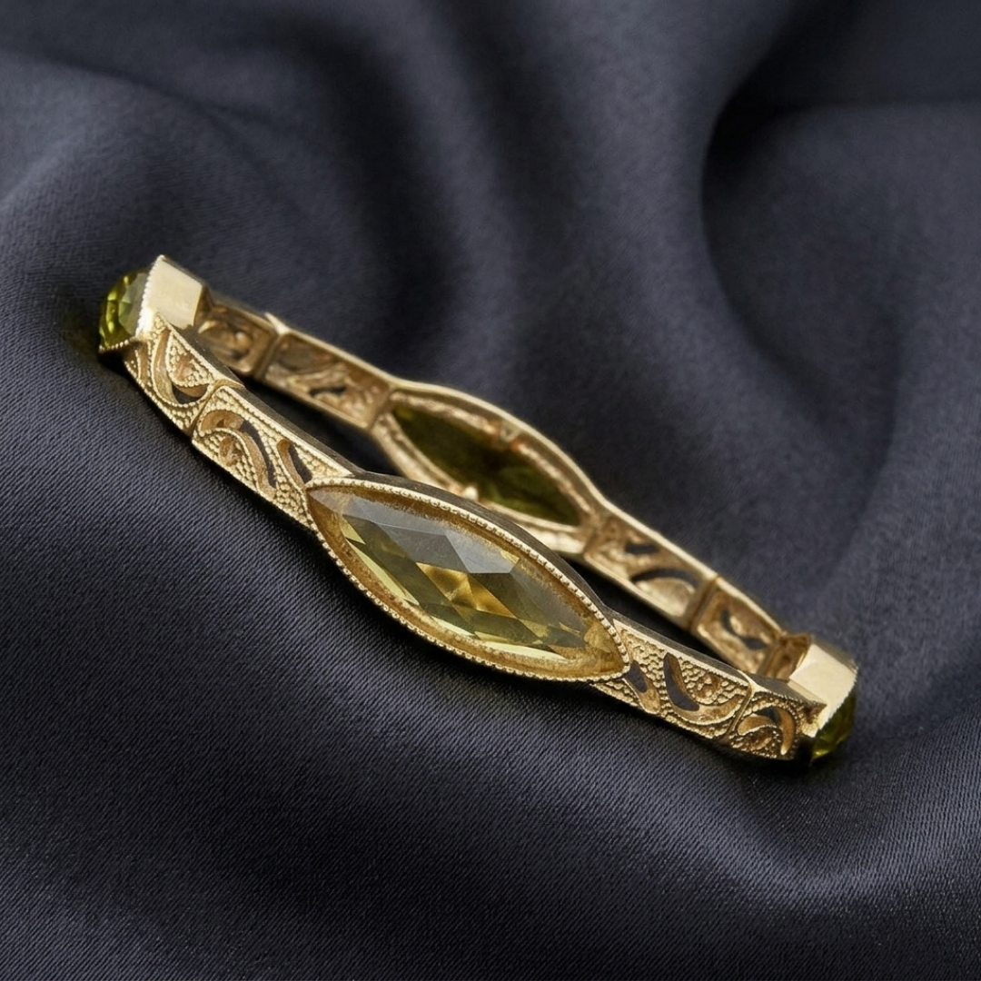 Gold bracelet with green crystal on a dark fabric background