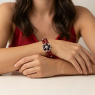 Woman wearing a red beaded bracelet with a floral crystal design on a plain background