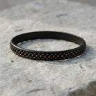 Black and gold bracelet with textured pattern on a stone surface