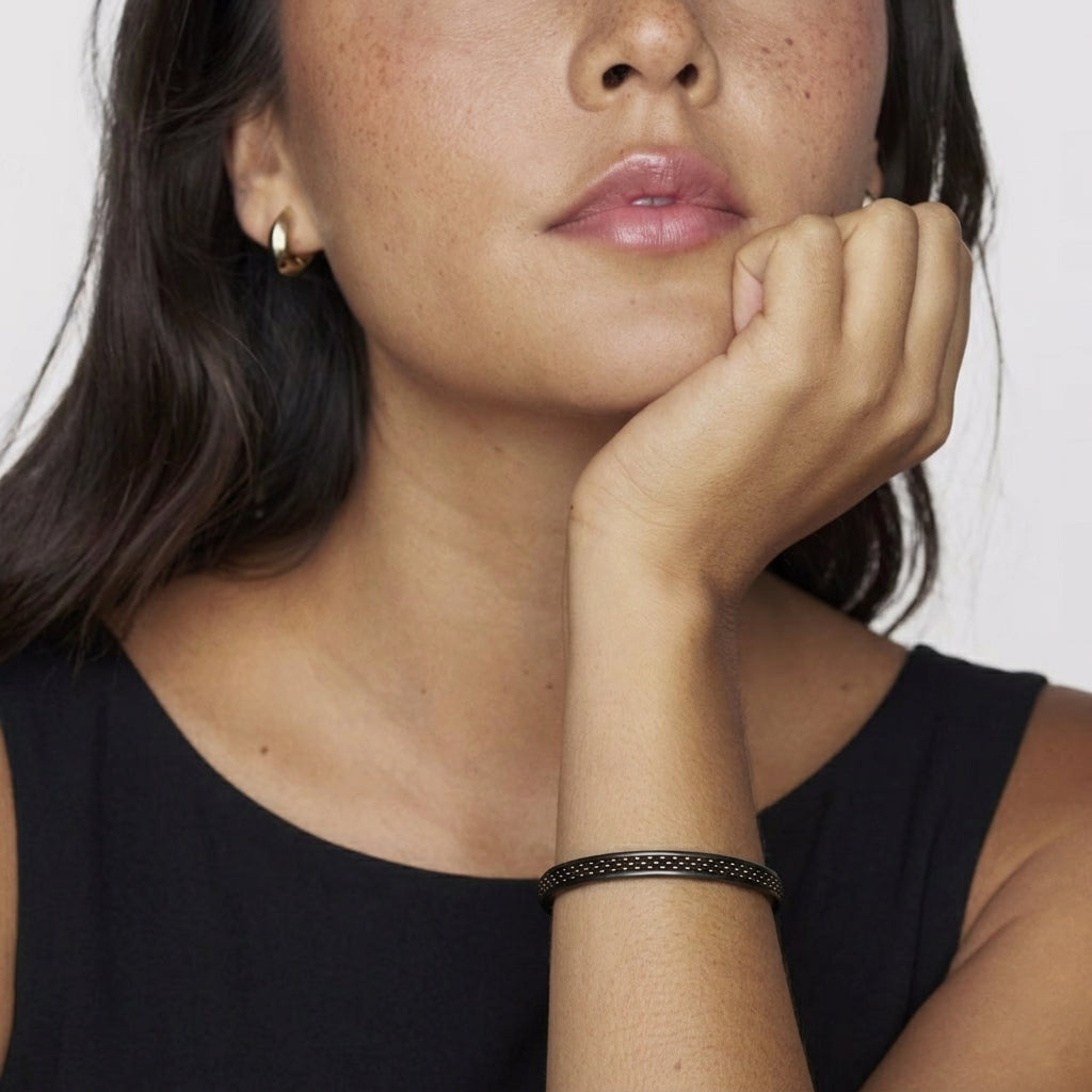 Close-up of a woman in a black dress and a black bracelet on her wrist with her hand on her chin against a white background