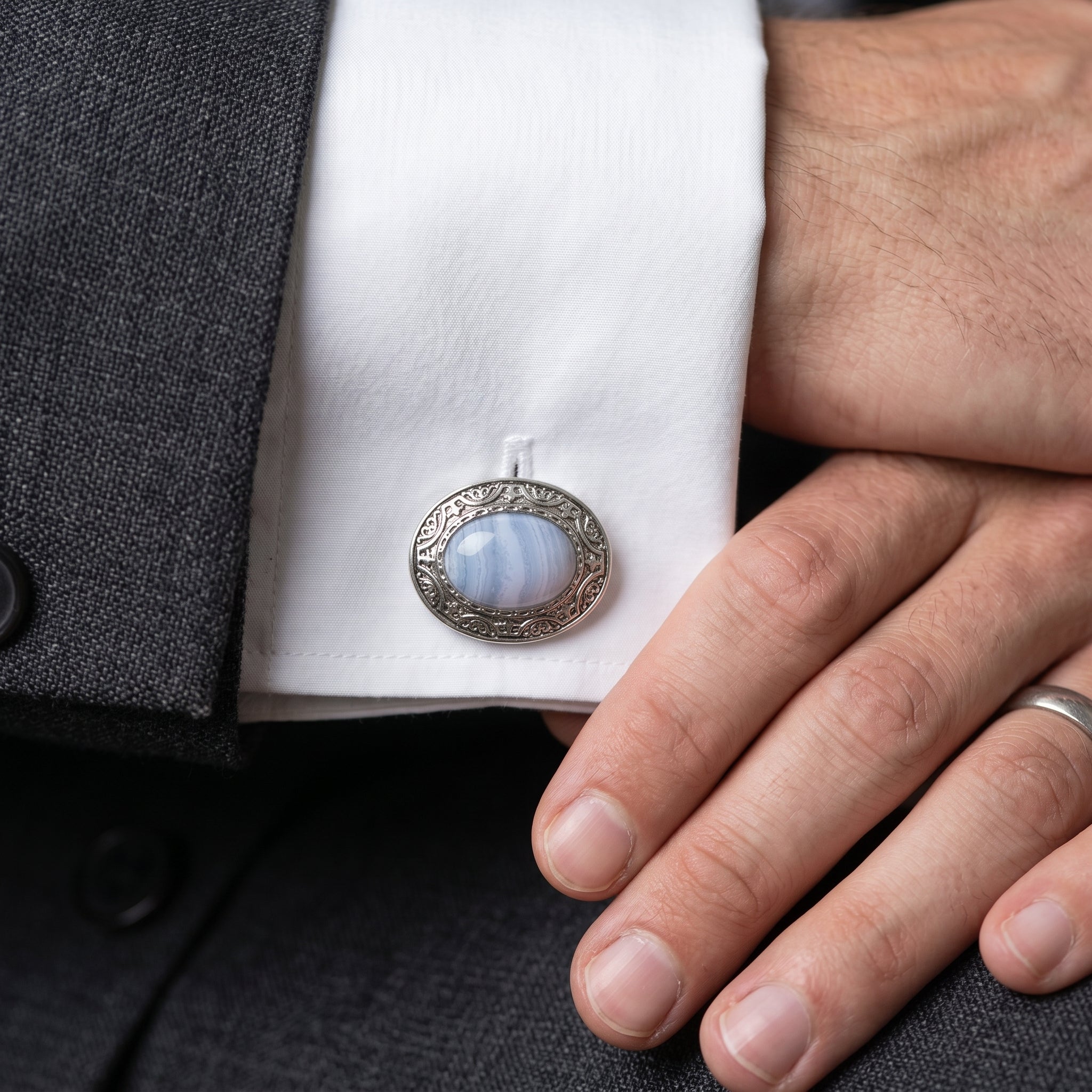Close-up of a light blue gemstone cufflink on a white shirt cuff with a dark suit jacket.