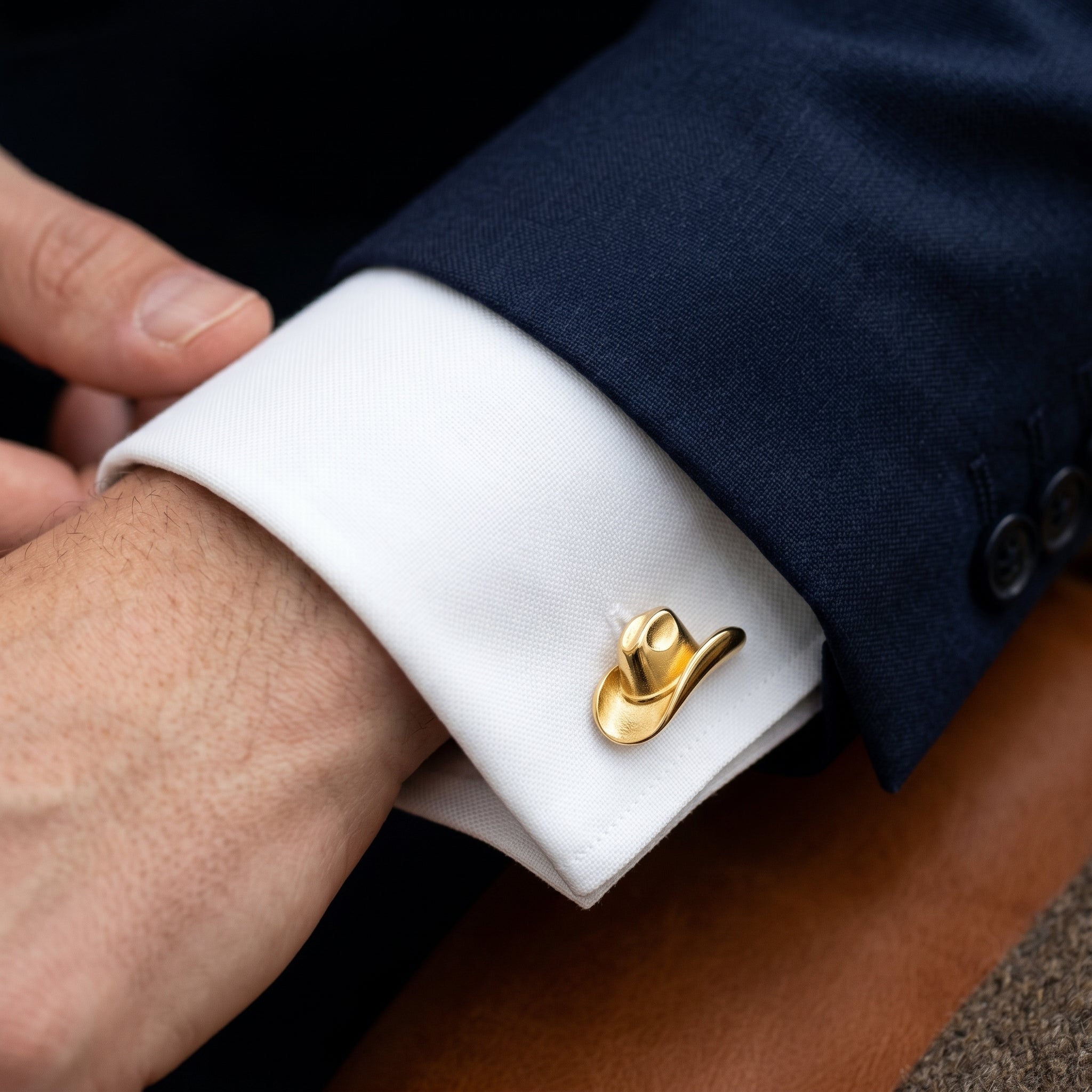 Gold cowboy hat cufflink on a white cuff against a navy suit background