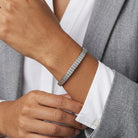 A close-up of a person's wrist wearing a silver tone link bracelet, styled with a white collared shirt and a gray blazer.