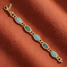 Gold bracelet with blue stones on a rust-colored fabric background