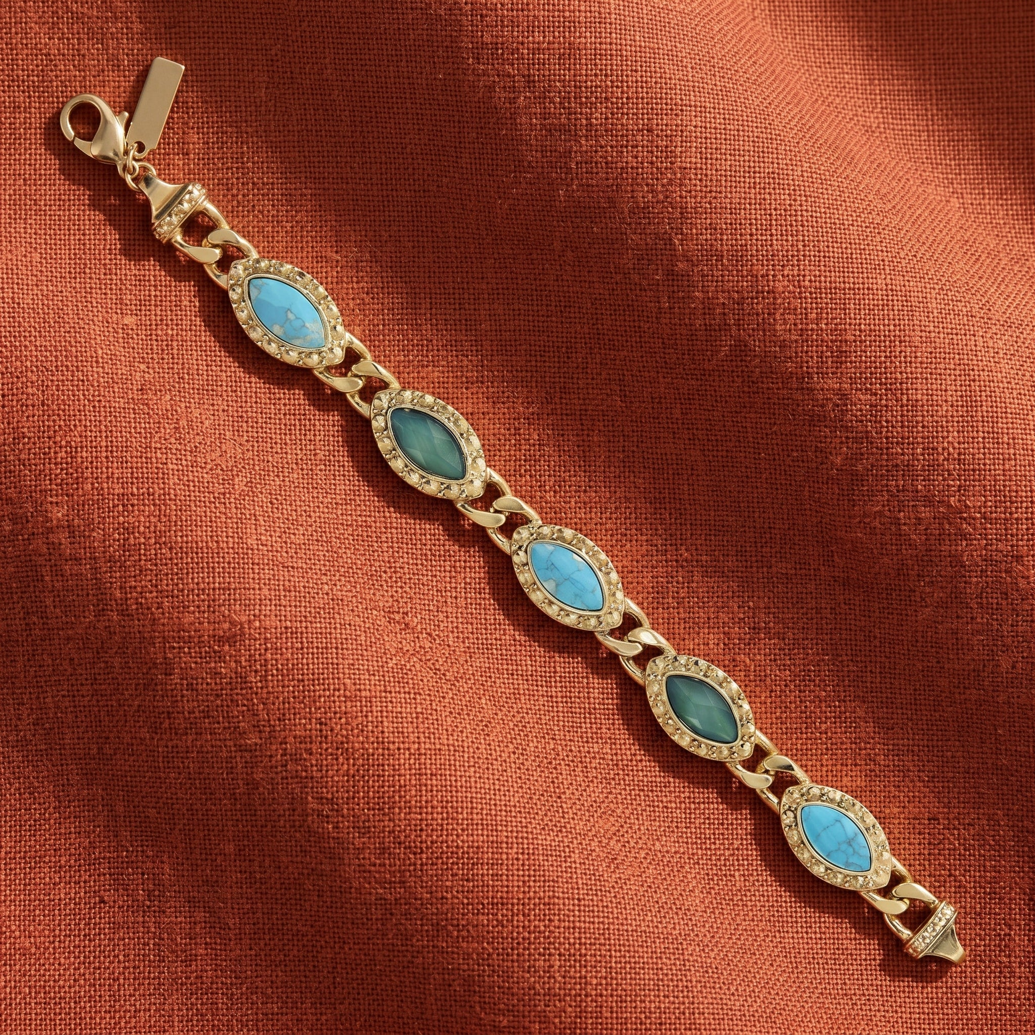 Gold bracelet with blue stones on a rust-colored fabric background