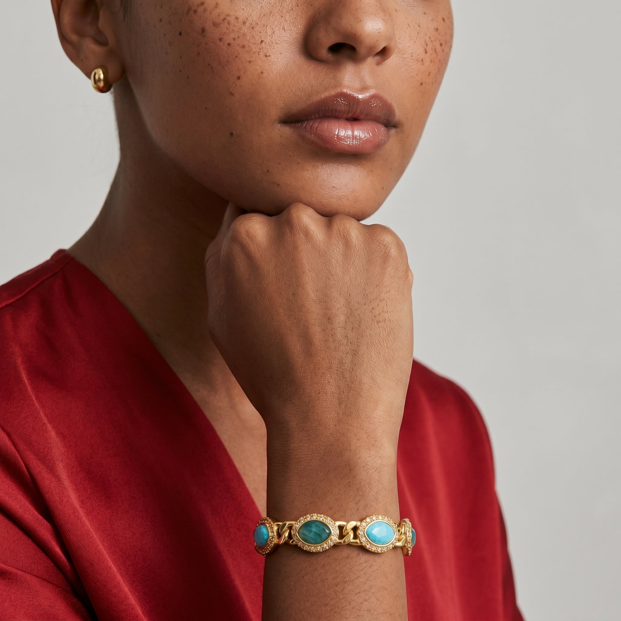 Woman wearing a gold bracelet with turquoise stones on a neutral background