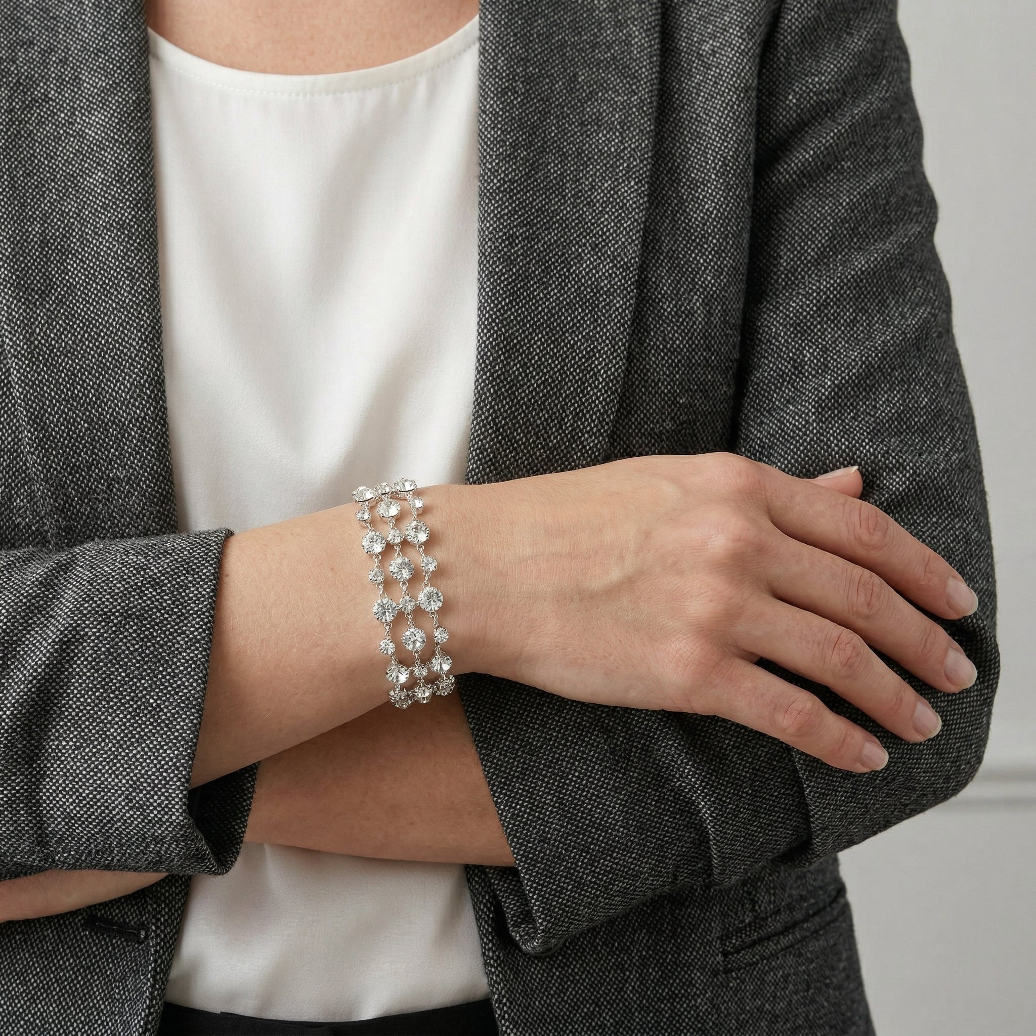 Person wearing a gray blazer and white shirt with a silver Austrian crystal bracelet on a neutral background