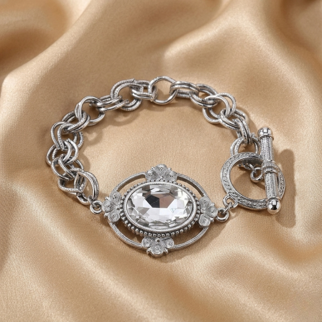Silver chain bracelet with a prominent clear crystal on a beige fabric background