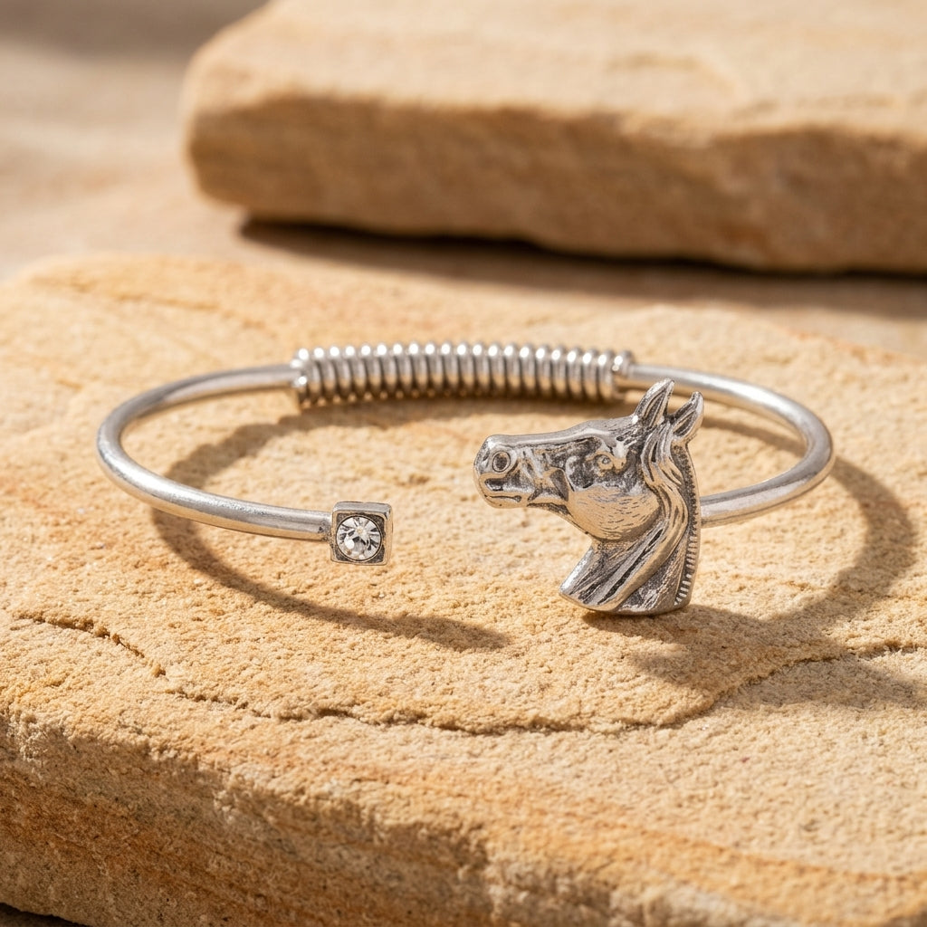 Silver tone horse head design spring cuff bracelet with a clear crystal accent resting on beige stone