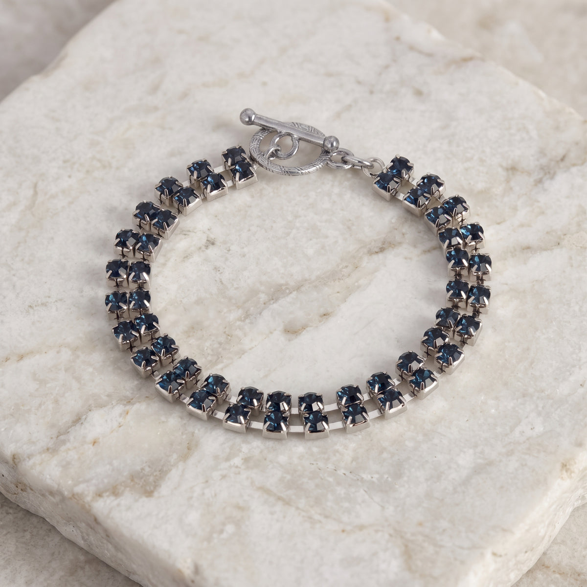 2-Row Radiant Crystal Blue Rhinestone Toggle Bracelet displayed on a textured white stone slab.