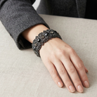 Decorative black bracelet on a person's wrist against a neutral background